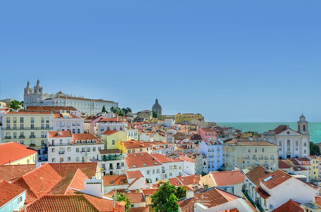 Vista panorámica del barrio de Alfama en Lisboa, con sus calles empedradas serpenteantes y edificios coloridos bajo un cielo azul.